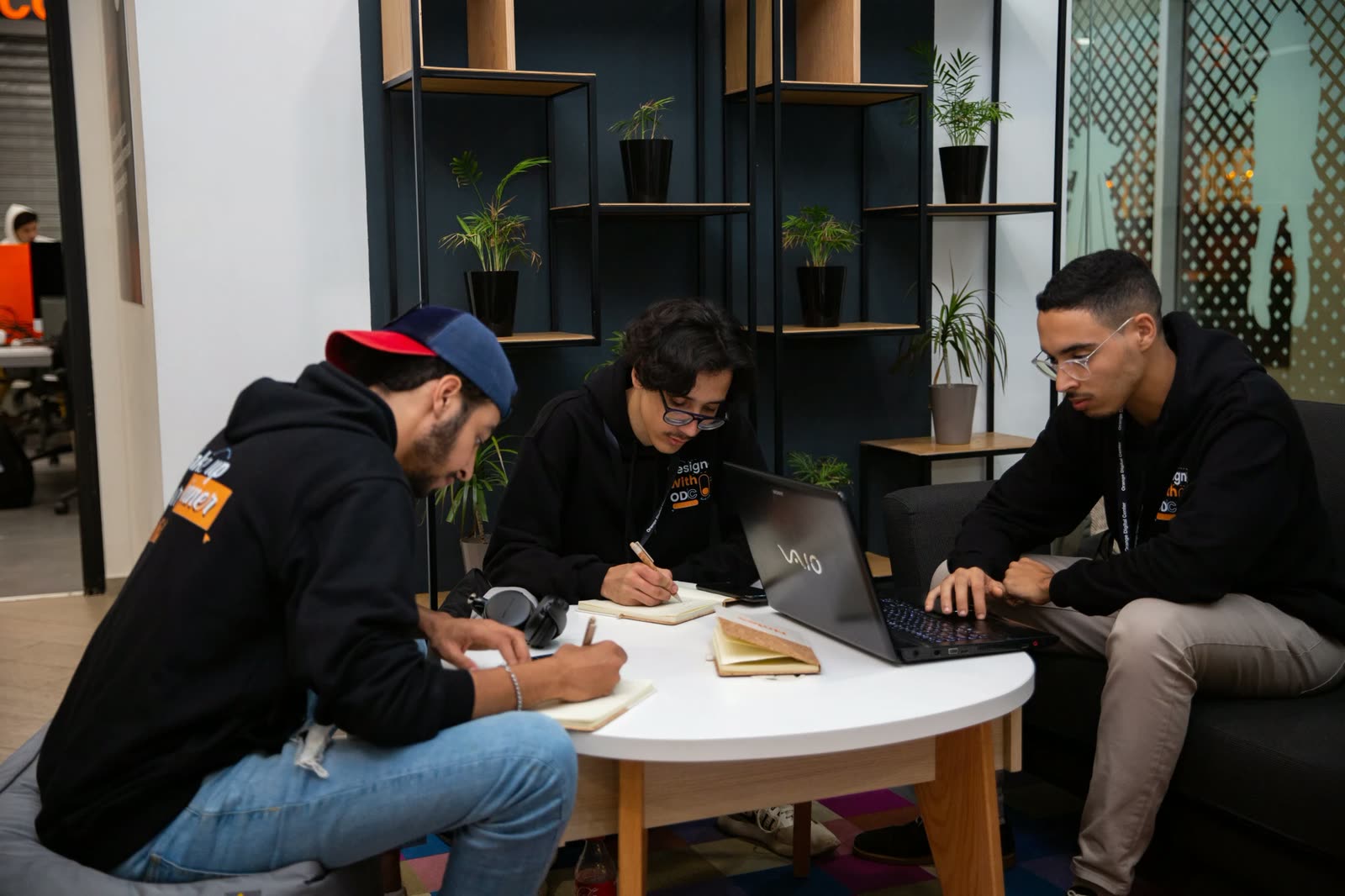 Trois designers travaillent ensemble autour d'une table, carnets et ordinateur
